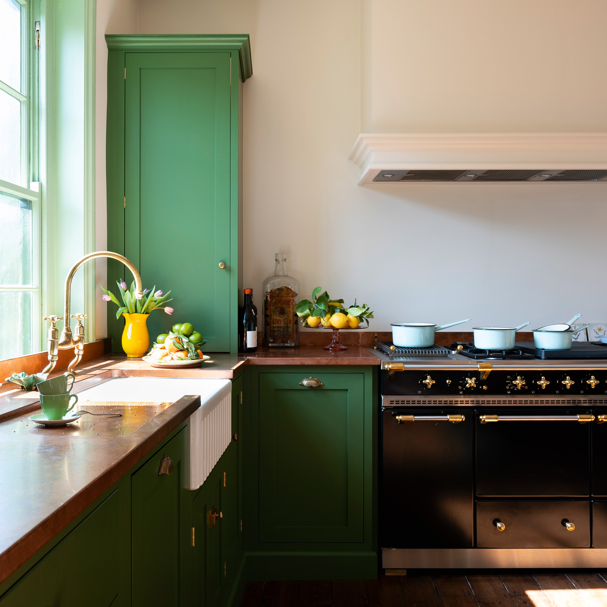 traditional kitchen with green cabinetry and woodwork, cream walls and wooden floors in 17th-century london maisonette looking towards black range cooker