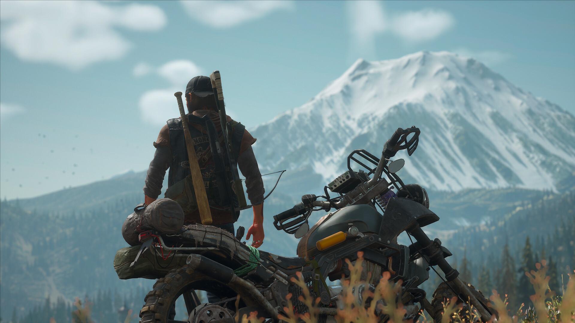 Days Gone Remastered protagonist Deacon standing by his bike and looking at a distant snowy mountain