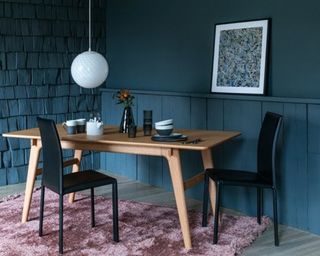 A wooden dining table with overdyed pink rug underneath, textured wall decor and Jackson Pollock framed art