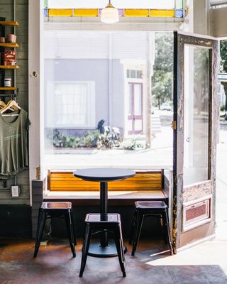 A sun-lit, retro-fueled cafe in New Orleans features an unfinished wooden door, cement flooring, and green wood paneled walls.