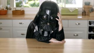 A boy dressed in a Darth Vader costume sits with head in hand