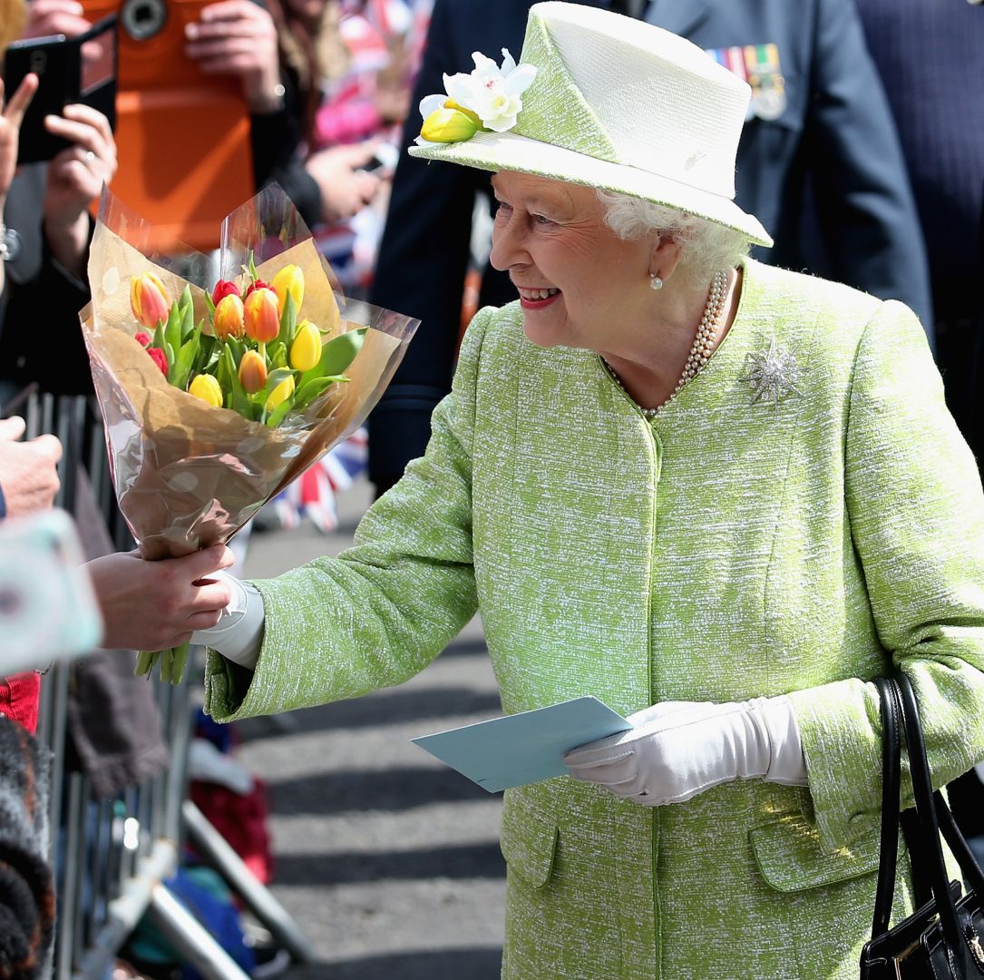 Queen Elizabeth wearing a green coat and taking a bouquet from a member of the public