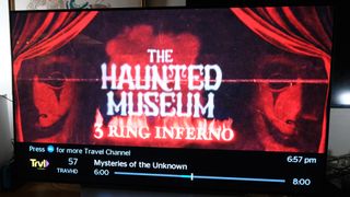 A Travel Channel ad for The Haunted Museum: 3 Ring Inferno on cable TV is seen on a TV connected to the Amazon Fire TV Cube (2022)