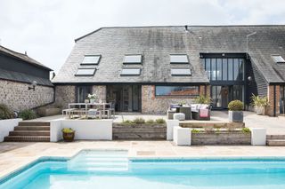 swimming pool with steps to outdoor dining and seating areas with low barn building in background