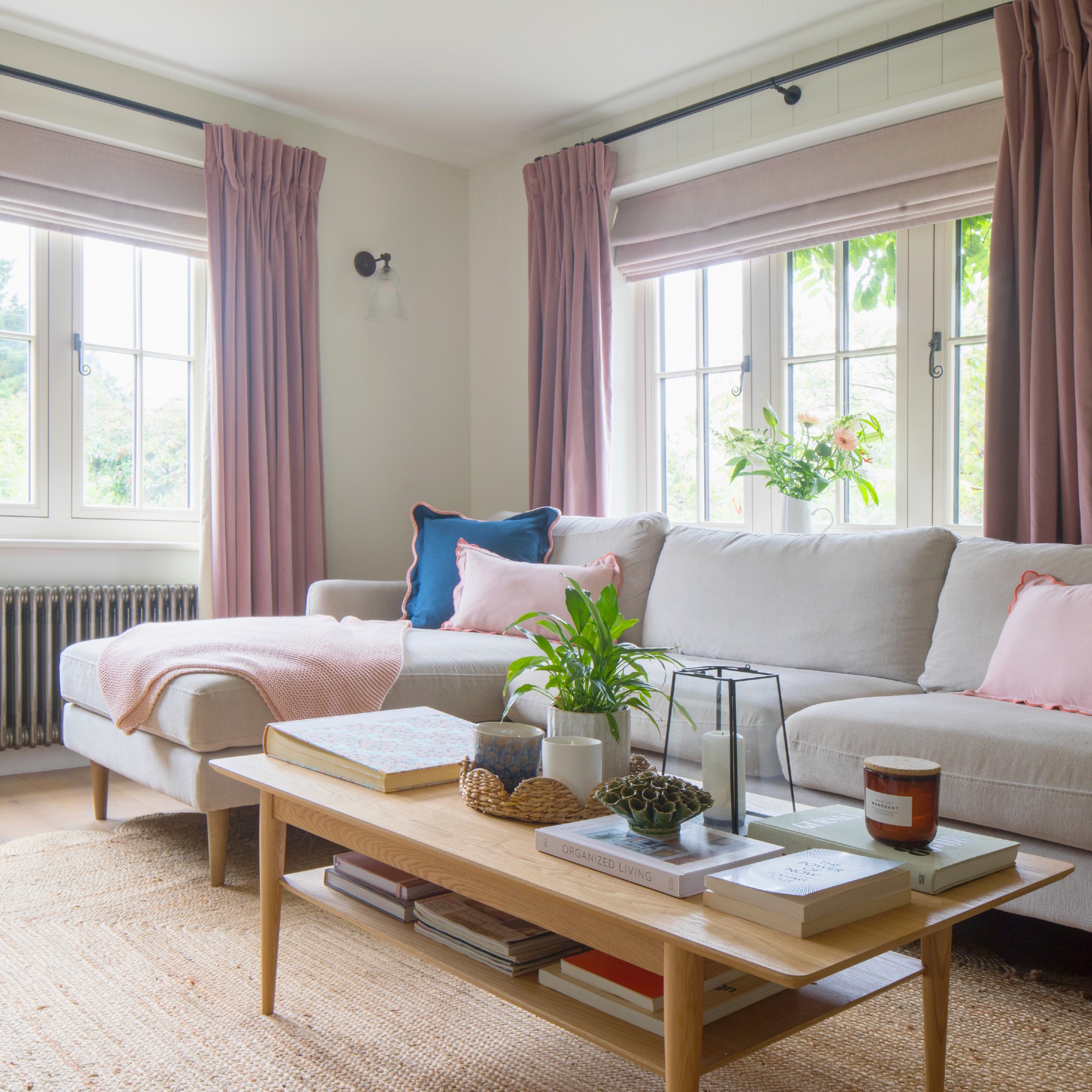 An off white-painted living room with a light grey chaise sofa and light pink accents through soft furnishings
