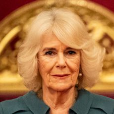 Queen Camilla has blonde hair and is wearing a dark green shirt dress