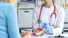 Gynecologist holds model of female reproductive system of uterus and consults patient. 