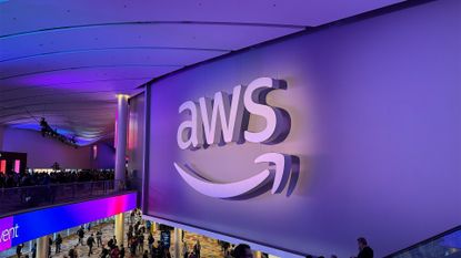 Amazon Web Services (AWS) logo pictured above an escalator at the Venetian Hotel conference center ahead of AWS re:Invent 2025 with conference attendees walking in foyer below. 