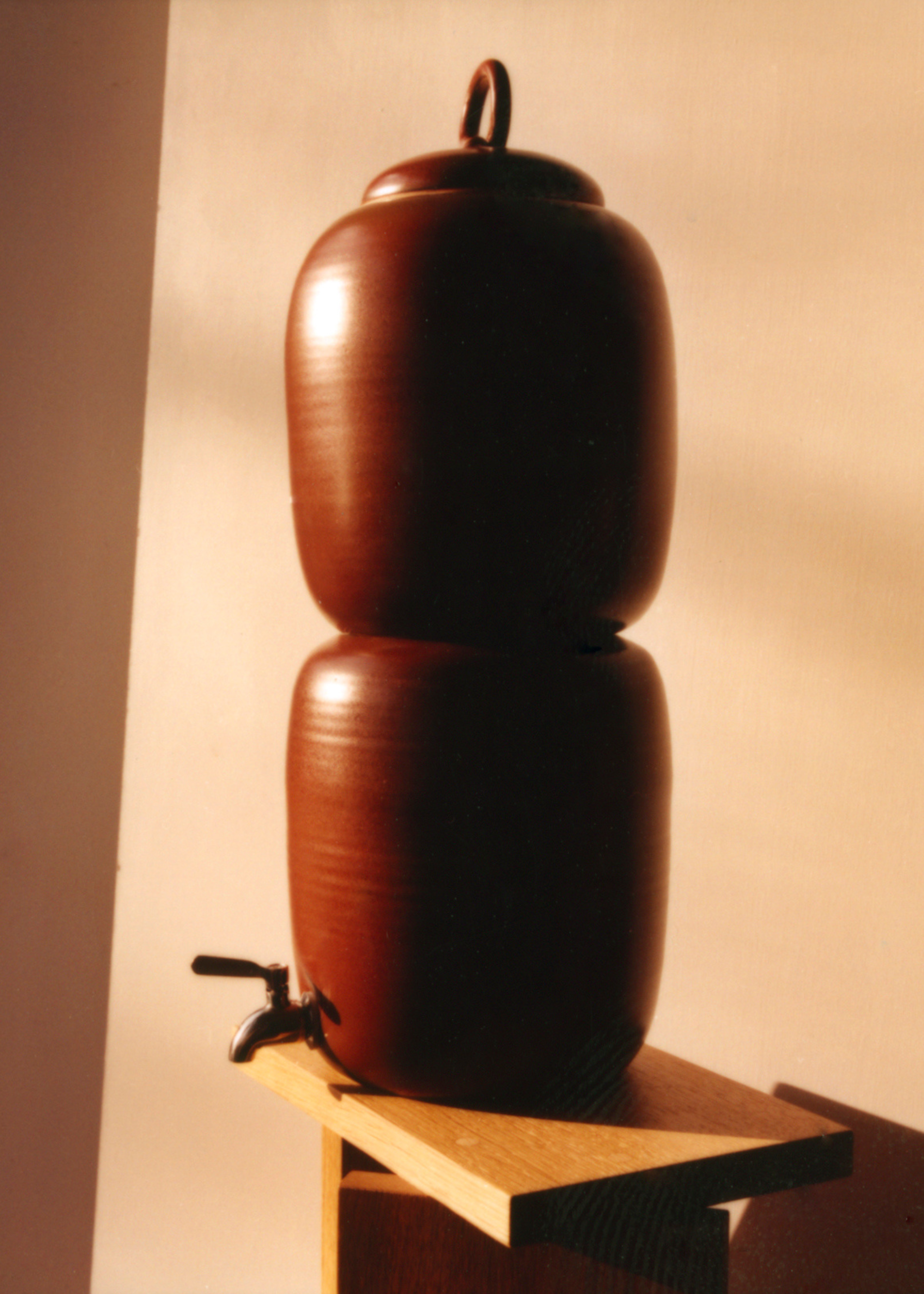A deep brown ceramic vessel on a wood side table in golden hour