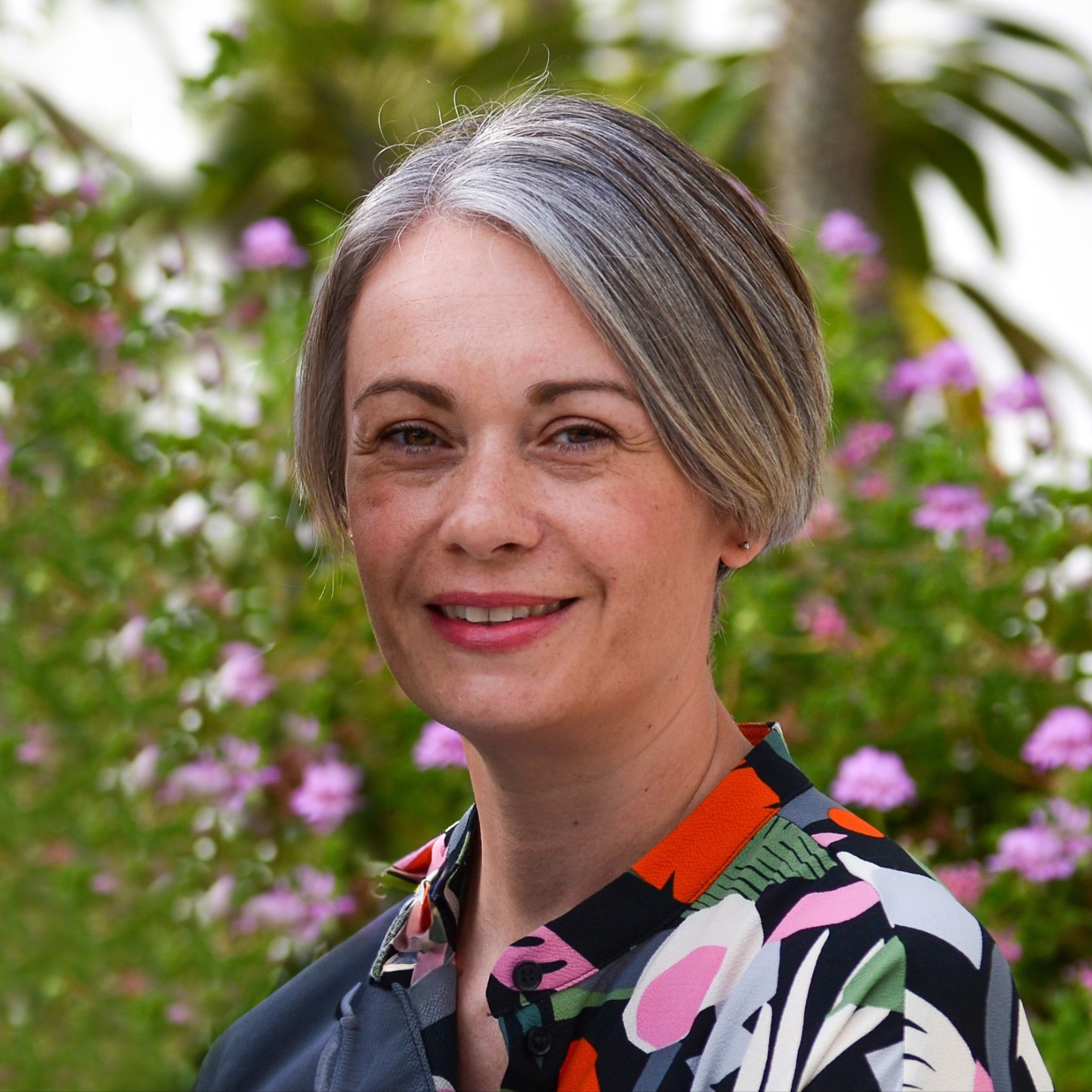 female with short grey bob stood outdoors wearing floral patterned top