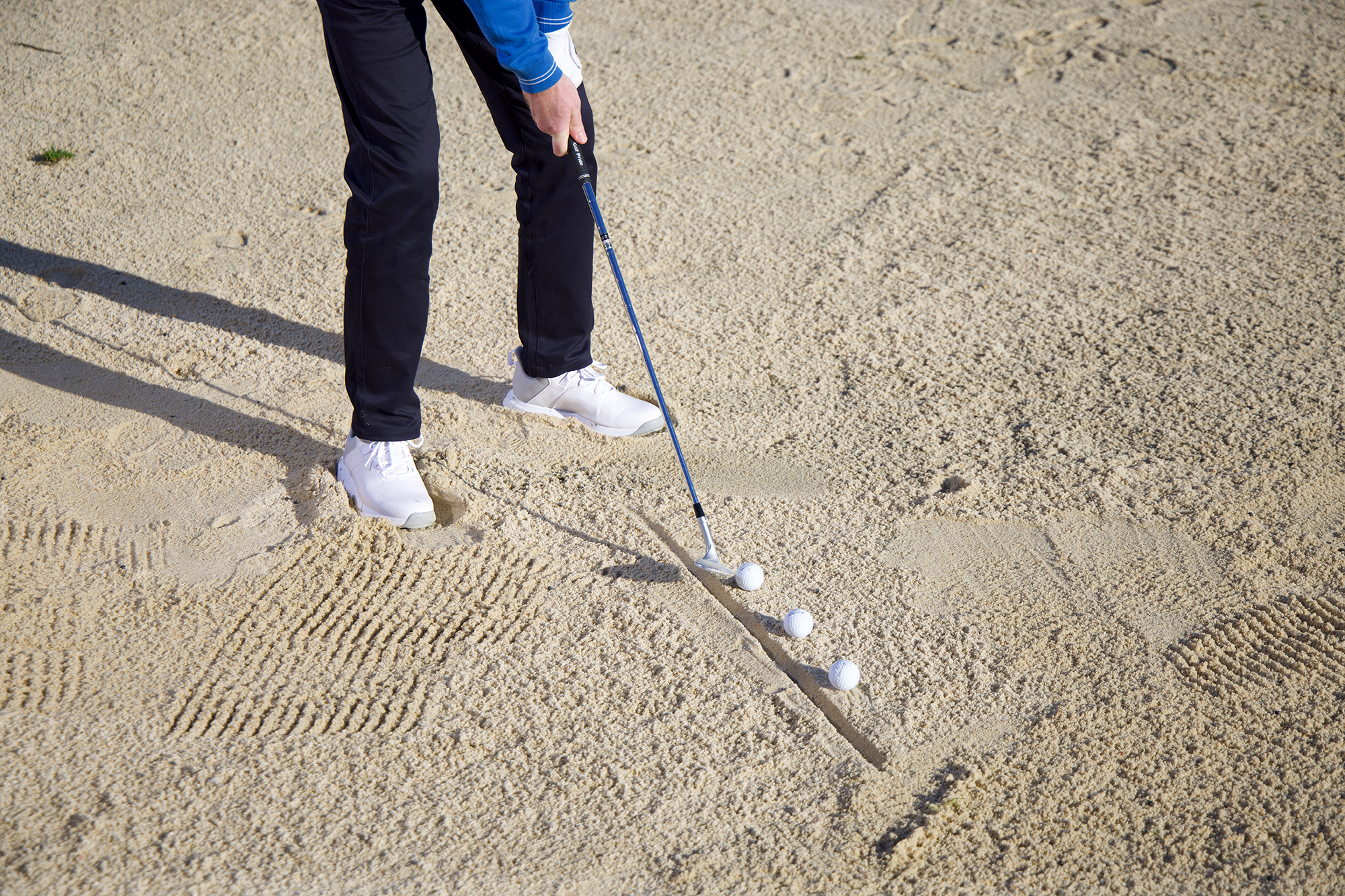 Keith Wood demonstrating a line drill for generating spin out bunkers, using three golf balls and a line drawn in the sand to indicate entry point with the club