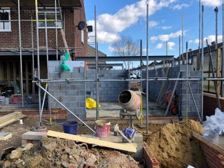 Blockwork being built up for an extension on a semi detached house with a yellow cement mixer in the foreground