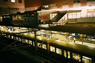 An aerial view of a train station captured with a passenger train on the tracks and graffitti on the walls of the station. Photographer at night
