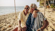 An older couple cuddle on a swing at the beach.