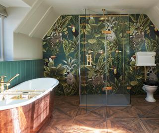 copper freestanding bath with green jungle style wallpaper, wooden floor and a large shower area with brass fittings