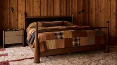 Image of a wooden bed with a patchwork quilt on it in a room that has wooden paneled walls. There is a white and red shag rug on the ground.