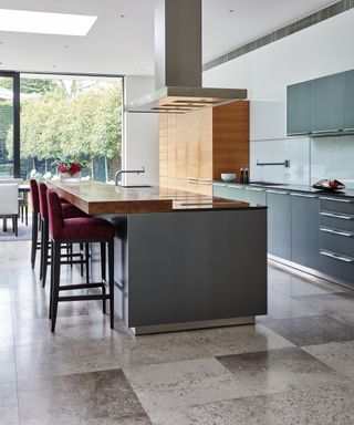A kitchen with grey granite floor tiles and a large island with plum bar stools