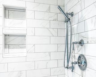 Photo of shiny clean tiled shower area with wall mounted silver fixtures and two built in, tiled cubbies for storage