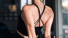 Rear view of woman stretching out back muscles in back exercises, wearing strappy sports top
