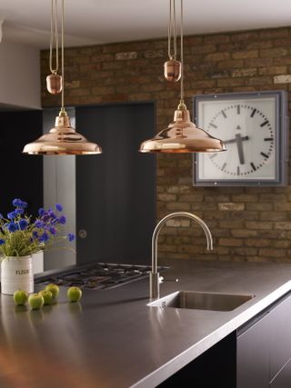 copper pendant lights above a kitchen island in a kitchen with exposed brick