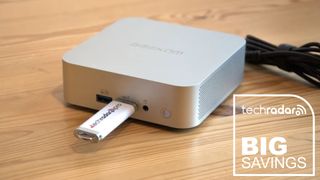 The Geekom A8 on a desk during our review, with a white TechRadar badge that reads 'Big Savings' in the lower right corner
