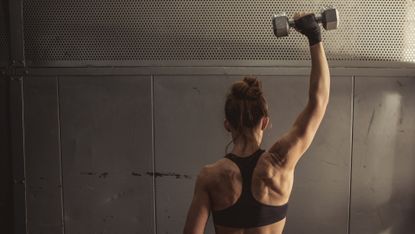 A strong and fit woman with her back to the camera lifting a weight above her head
