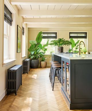 neutral kitchen with dark gray island, herringbone wooden floor, wooden barstools and dark gray radiators