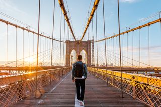 Young man walking on the Brooklyn Bridge at sunrise, New York, USA