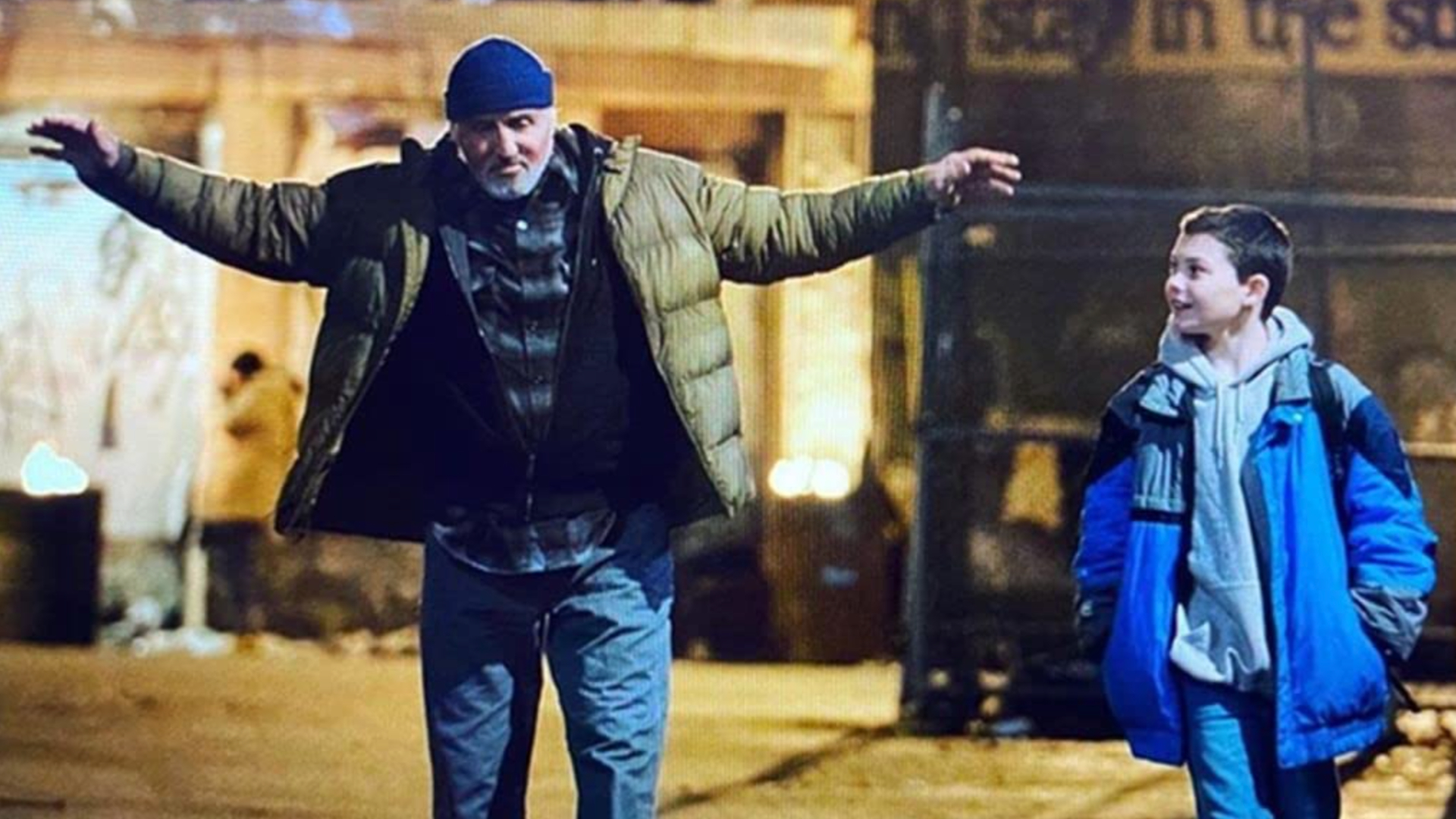 A still from the movie Samaritan (2022). An older man and young body are walking around a dirty street, both wrapped up in big, warm coats.