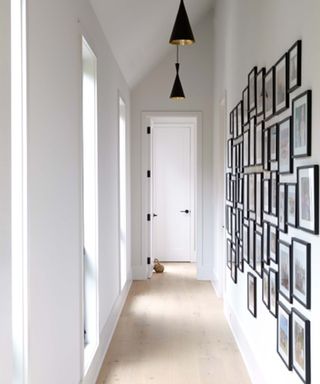 White narrow hallway with light wood floor, and family photo wall feature with matching black frames.