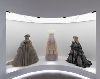 Gallery view of The Met’s Sleeping Beauties Reawakening Fashion, featuring trio of ball gowns in curved gallery