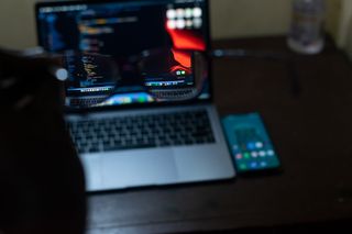 person holding glasses up to focus on MacBook on desk