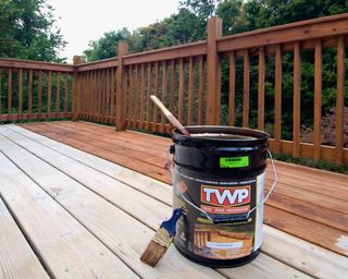 Five Gallon Bucket of Wood Stain and Preservative on Partially Stained Deck