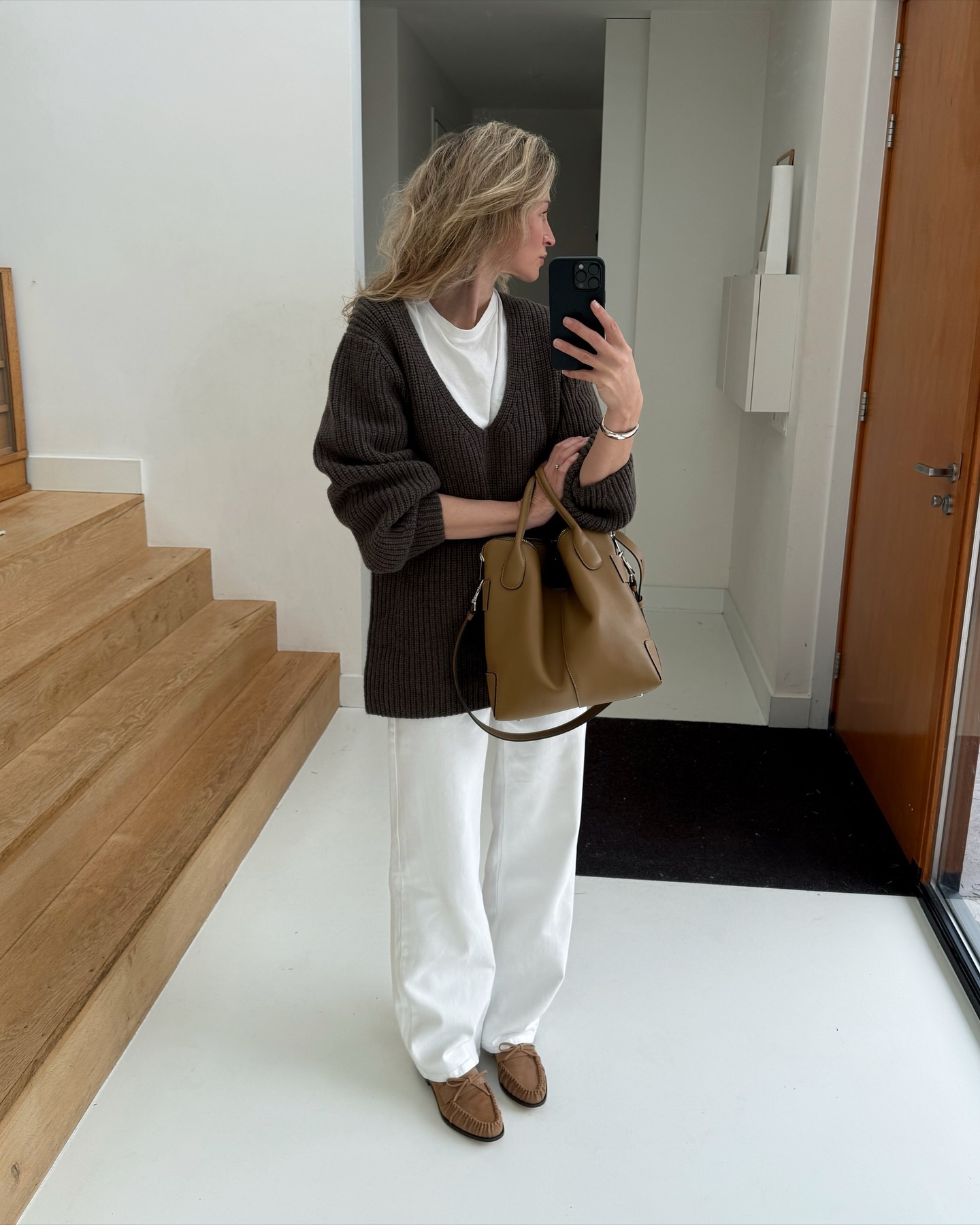 Woman wearing a brown v-neck sweater over a white tee and white jeans.