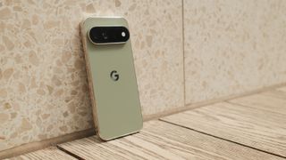 Google Pixel 11 Pro XL leaning against a light stone wall on a wooden floor, showing its rear design and camera bar.