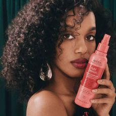 A model holding an Aveda product in her hand next to her face.