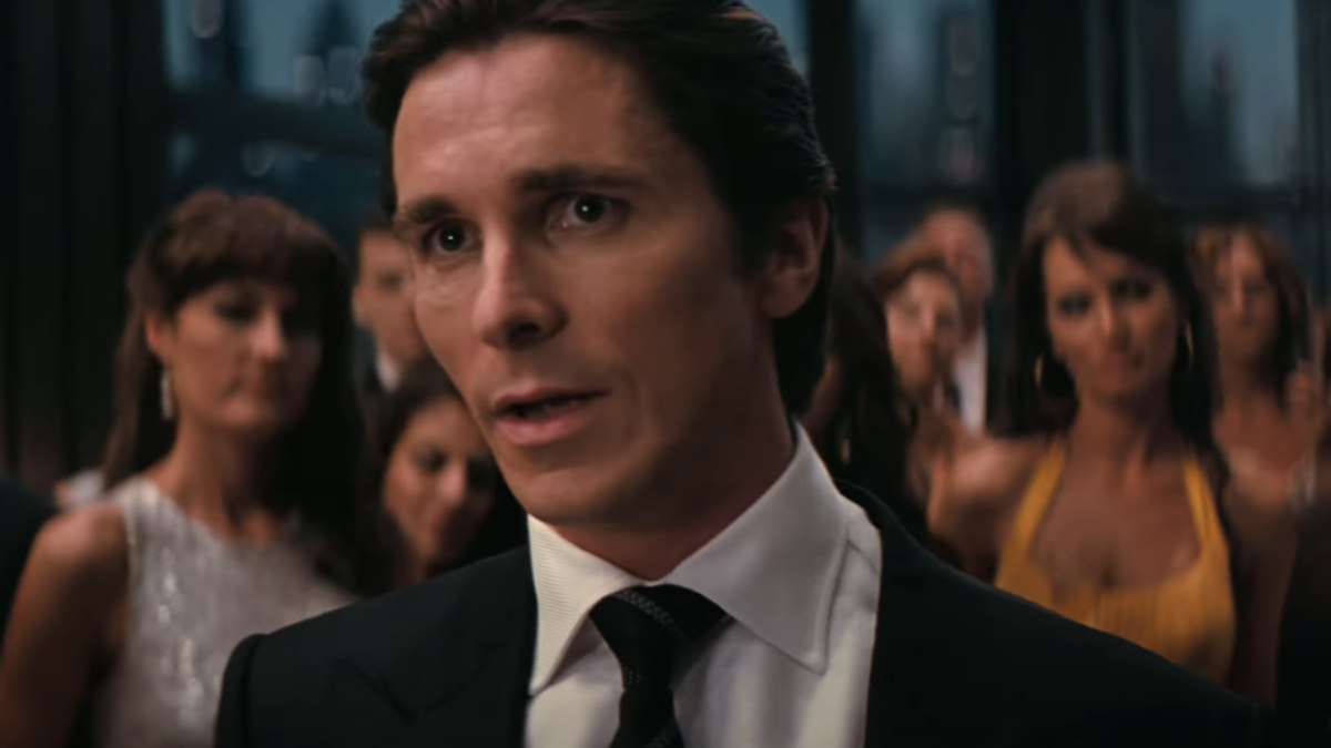 Christian Bale talking in a suit at a party in The Dark Knight