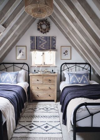 Twin beds with blue cushions in loft space with beams and rooflight