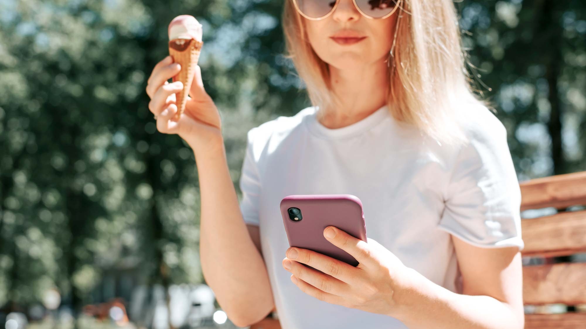 Женщина с мороженым держит телефон в солнечный день