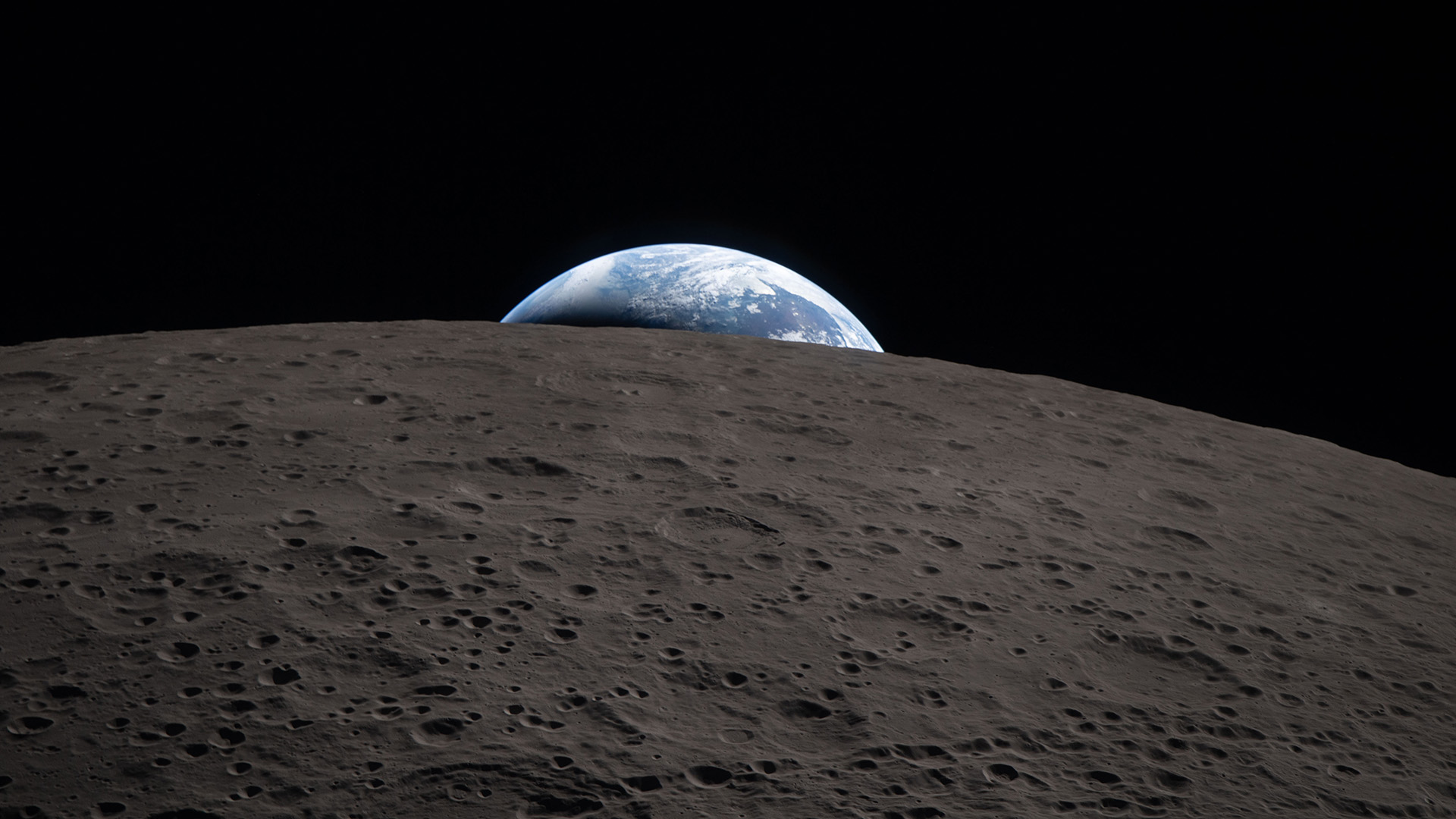 A view of the blue and white Earth setting behind the curved, gray horizon of the moon.