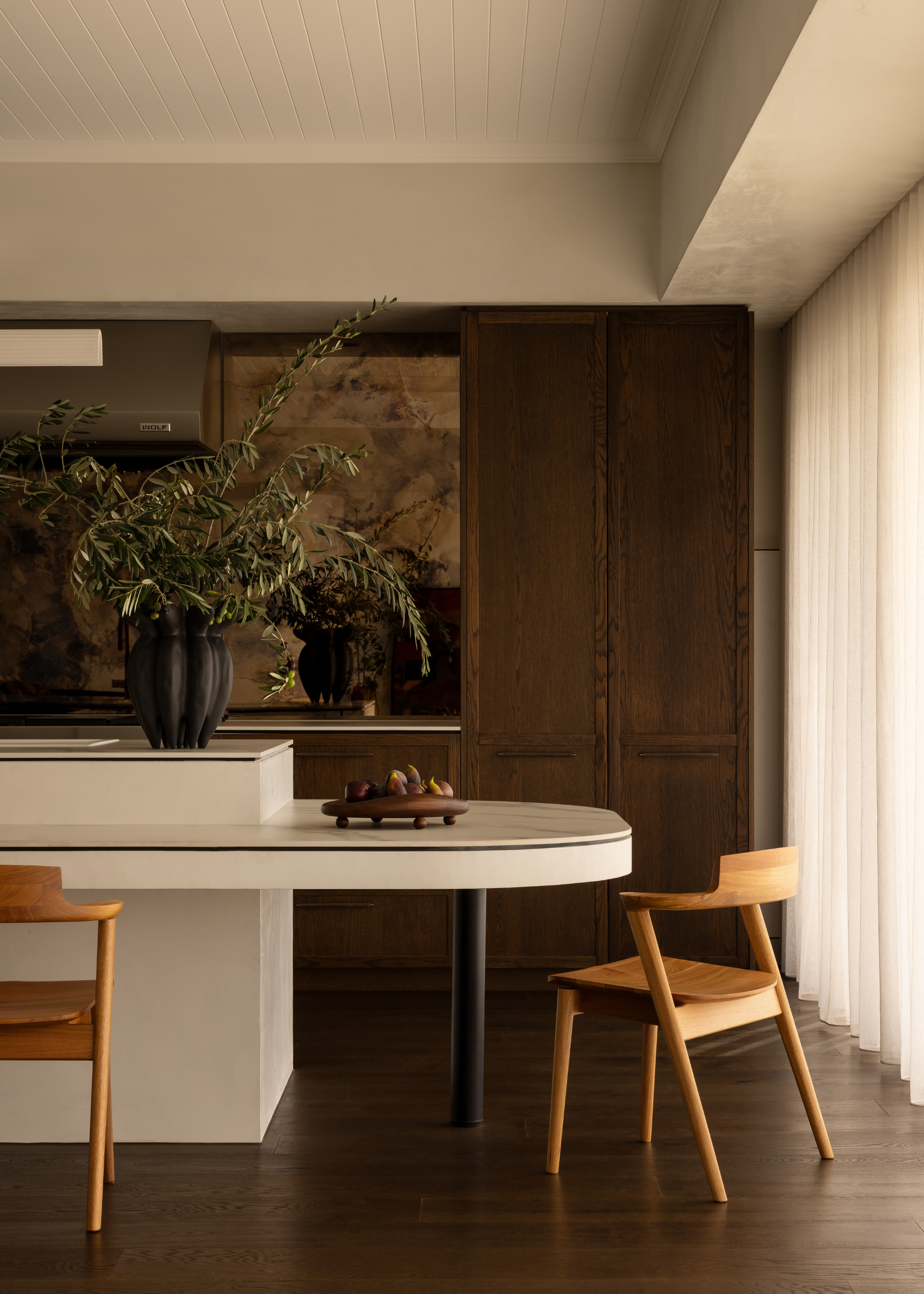 An open kitchen with a white island and extension beside wooden chairs