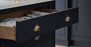 Navy blue kitchen drawers with brass clasp handles to show how to make a kitchen look expensive on a budget by adding luxe handles