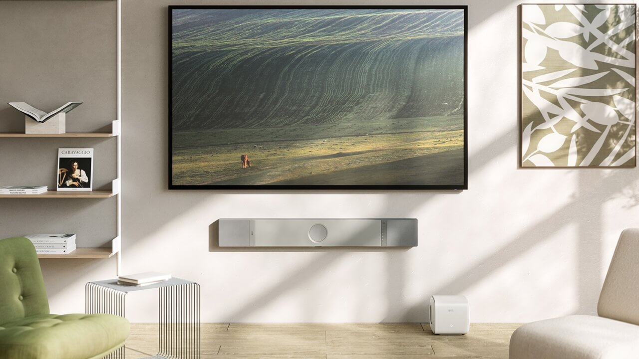 A lifestyle image showing a KEF XIO soundbar wall-mounted below a large TV. The TV is showing a landscape and the room is decorated in neutral colours