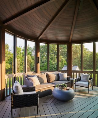 Large outdoor terrace, porch area, paneled dark wooden ceiling in a rounded structure, dark wooden floor, outdoor sofa and armchair, rounded side table