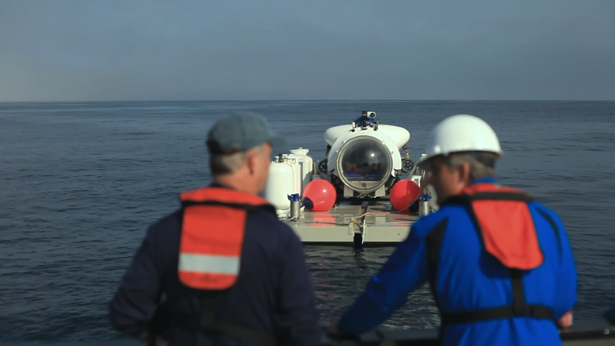 Two men oversee the Titan submersible floating on buoys in the water