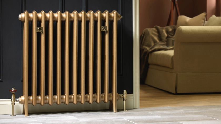 Gold column radiator in front of a dark wall with a sofa in the background