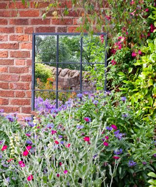 Outdoor mirror on a red brick wall with flowering perennials