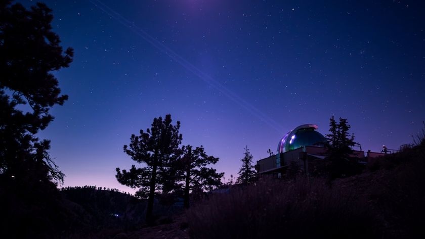 The purple and blue night skies glow over an observatory that shoots faint light beams across the sky
