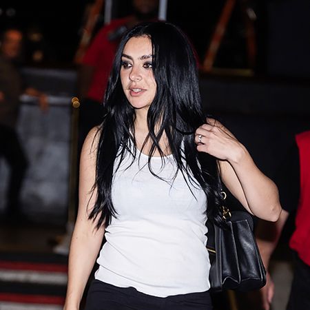Charli xcx wearing a white tank top, black cropped pants, and black heels