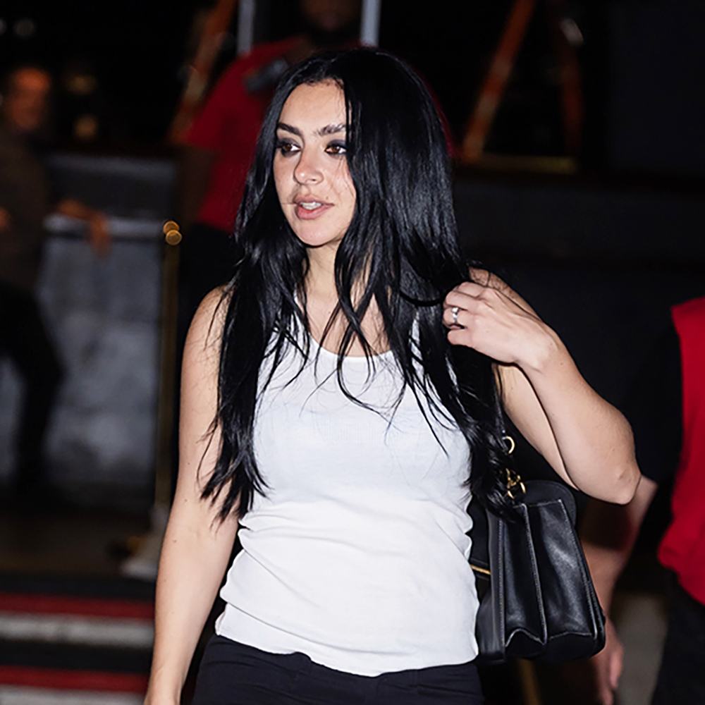 Charli xcx wearing a white tank top, black cropped pants, and black heels
